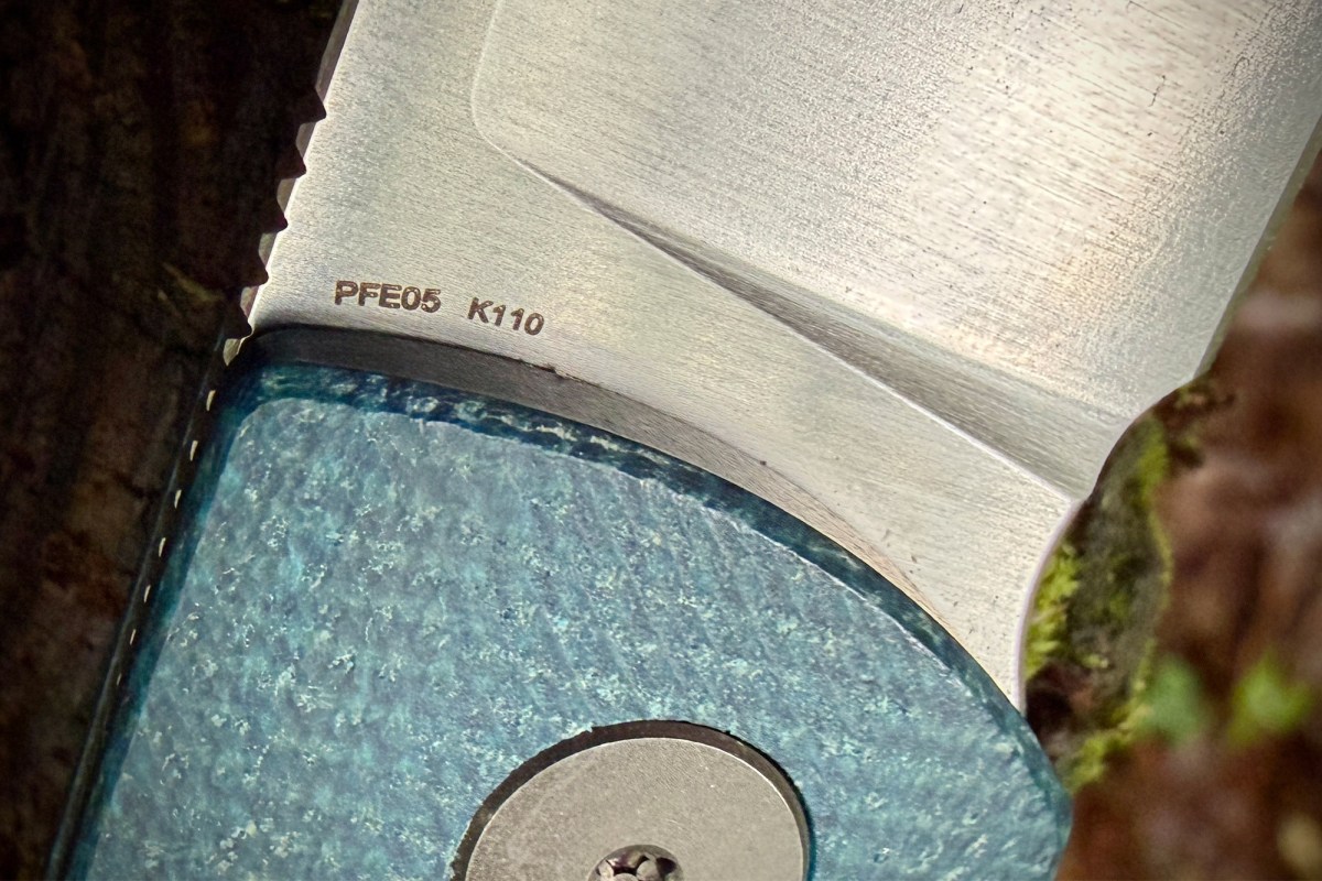 Close-up of the Flavorist blade markings and teal handle scale on a mossy surface