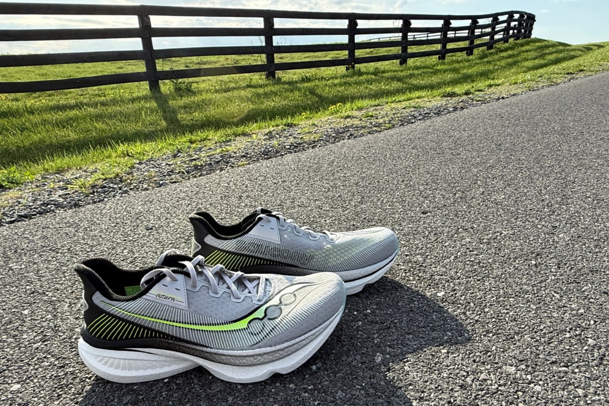 Gray running shoes on pavement near a black fence and grassy field