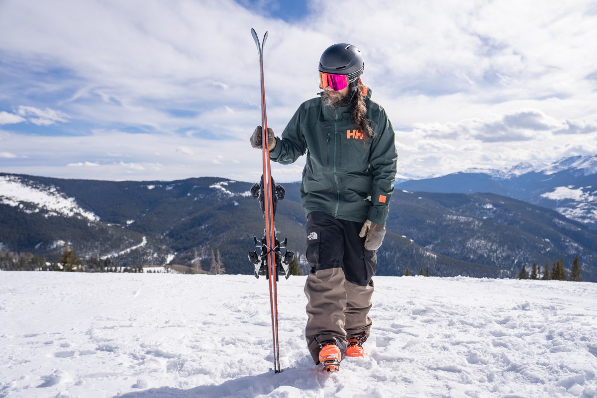 Skier wearing the HH Ridge Infinity Jacket 2.0 carries skis across a snowy mountain ridge