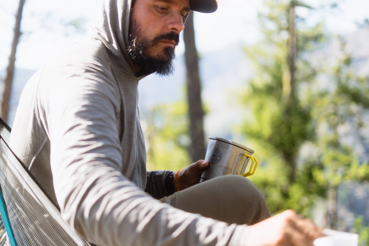 A camper holds the Highcountry cook pot while sitting in a camp chair