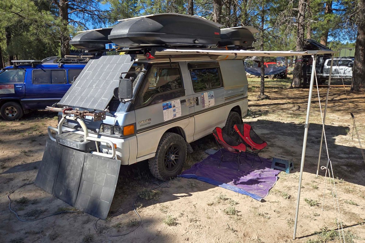 Mitsubishi Delica camper with solar panels, roof storage, and an awning set up under trees