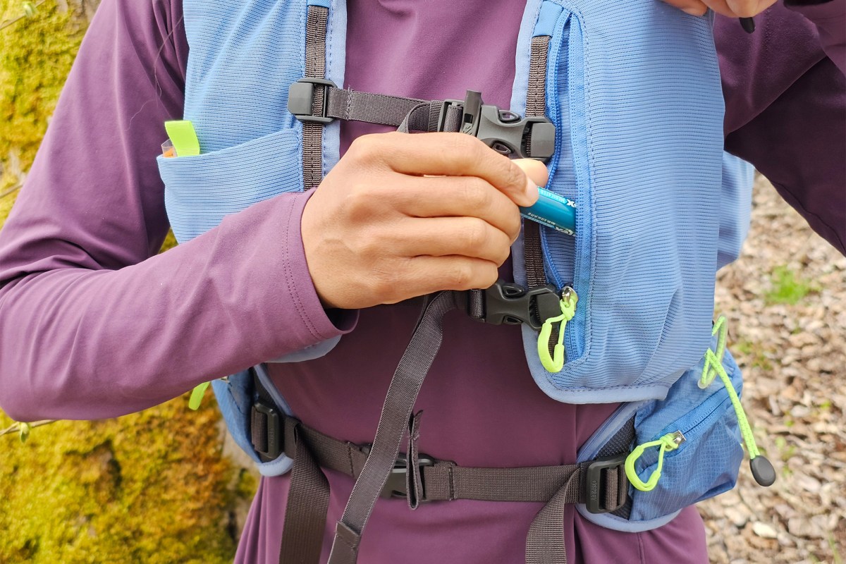 A hiker reaches for an energy gel in the front pocket of a blue Osprey pack