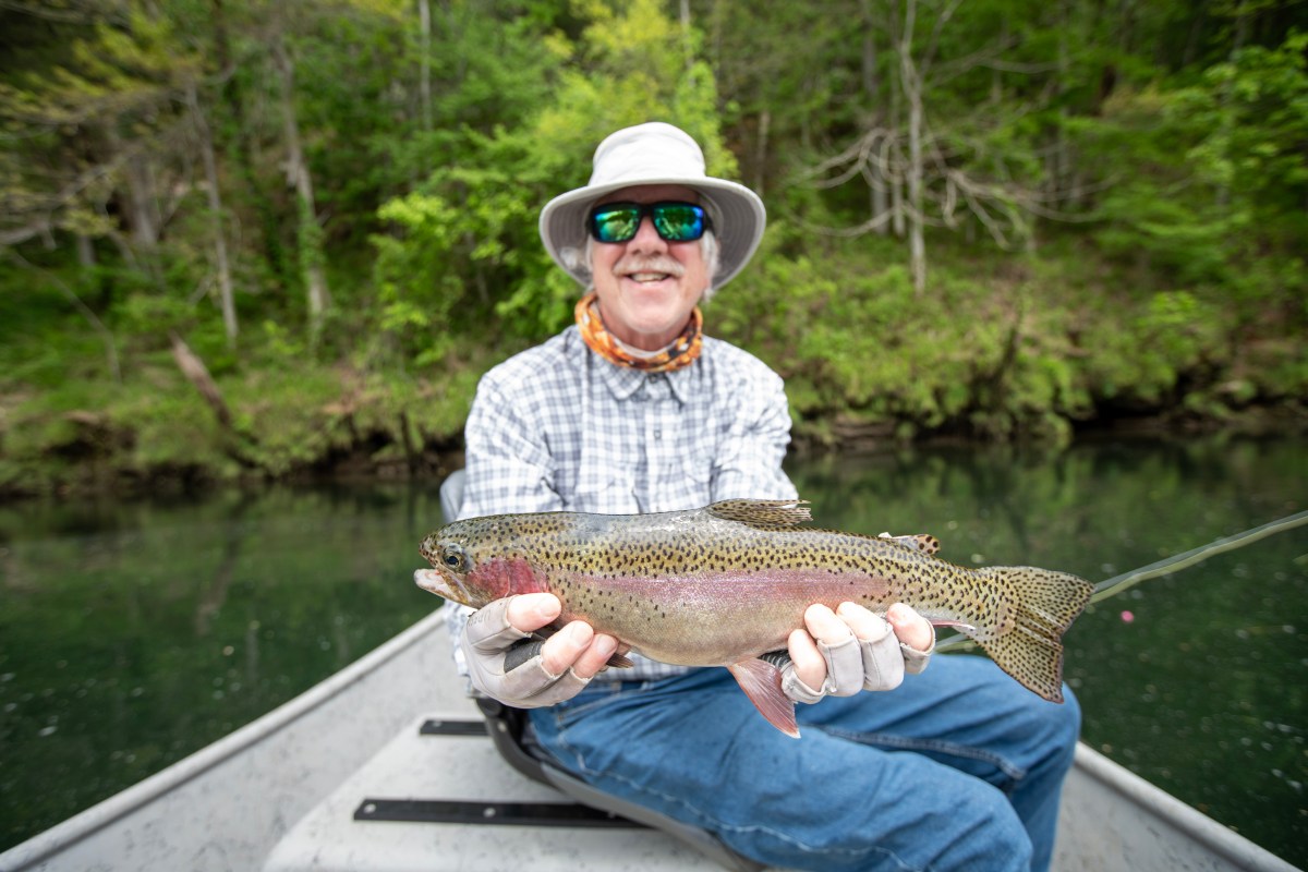 An angler on the front of a drift boat holding a rainbow trout.