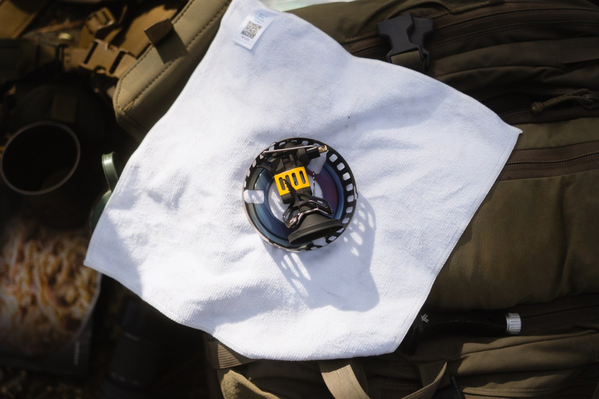 The stove burner and removable windguard sit on a cloth over a backpack