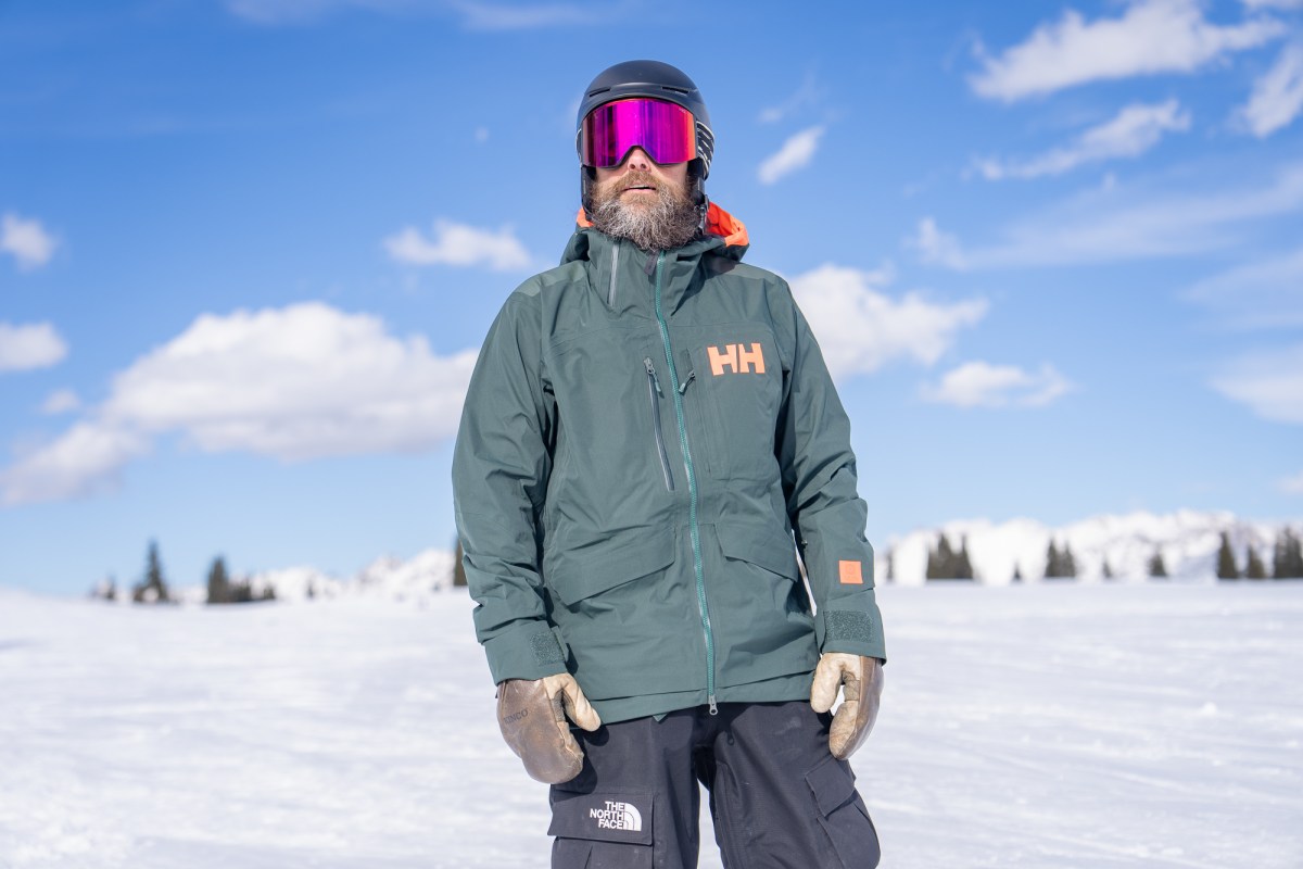 Skier wearing the Ridge Infinity Jacket 2.0 stands on a snowy mountain under a blue sky