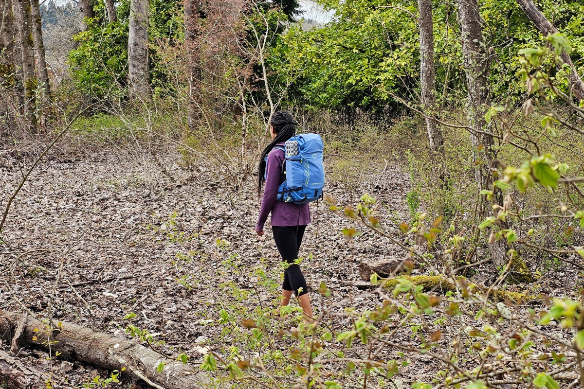 A hiker walks through the forest wearing a blue Tempest Velocity 30 backpack
