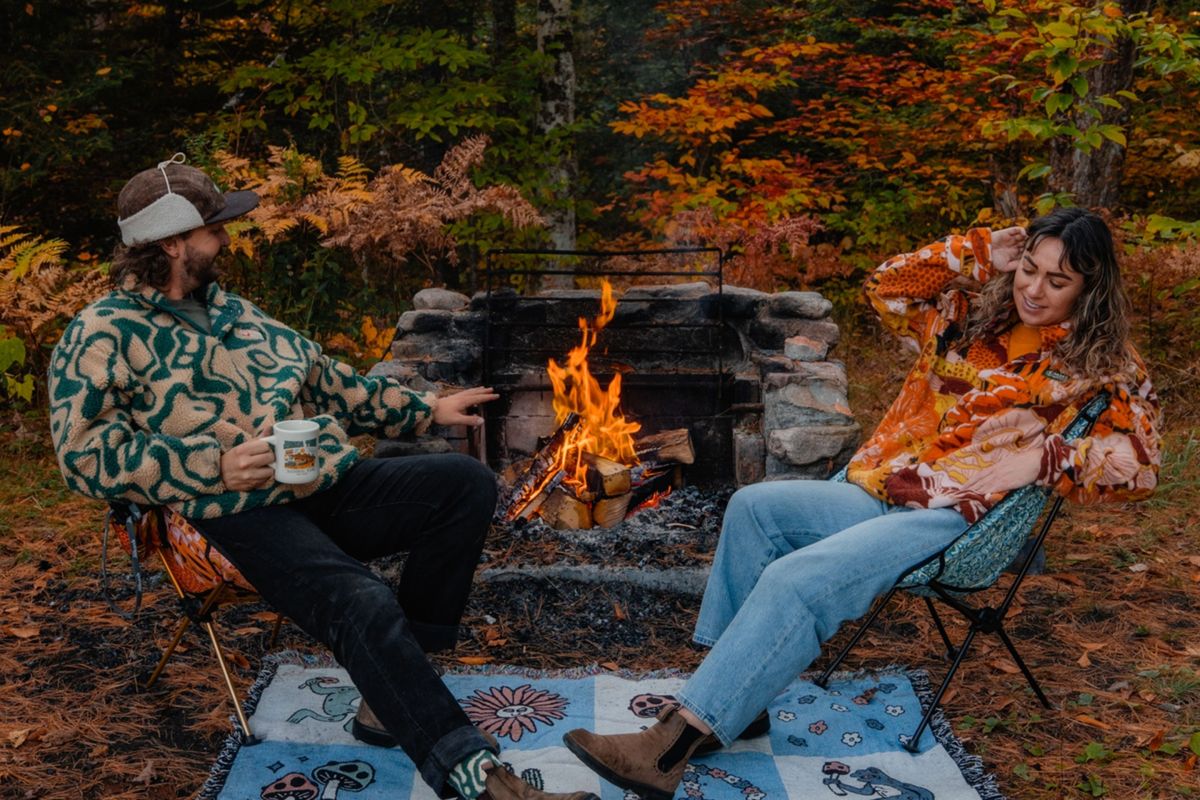 2 people sit in chairs around a campfire