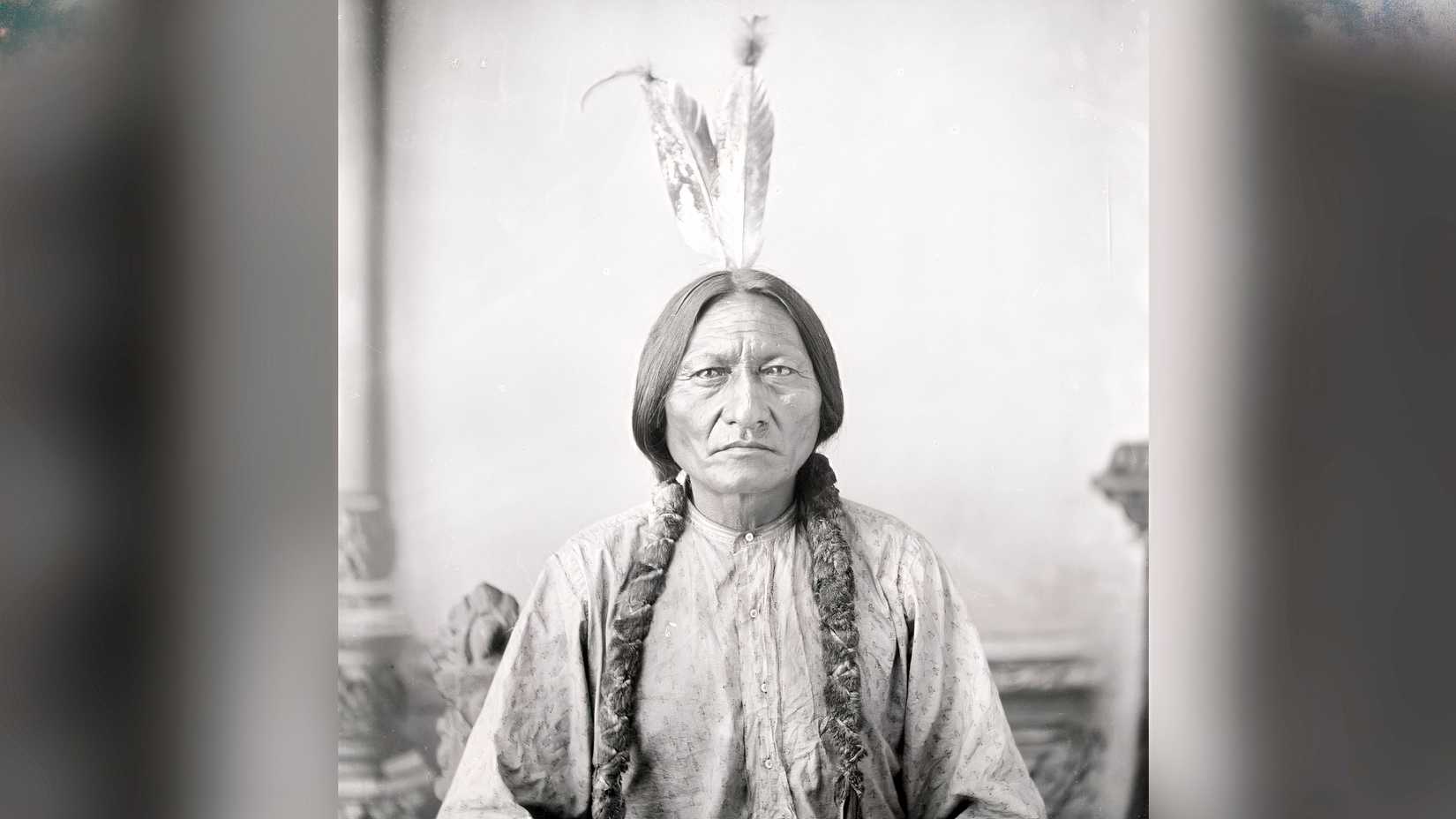 A black-and-white portrait of Sitting Bull wearing braided hair and a feather.