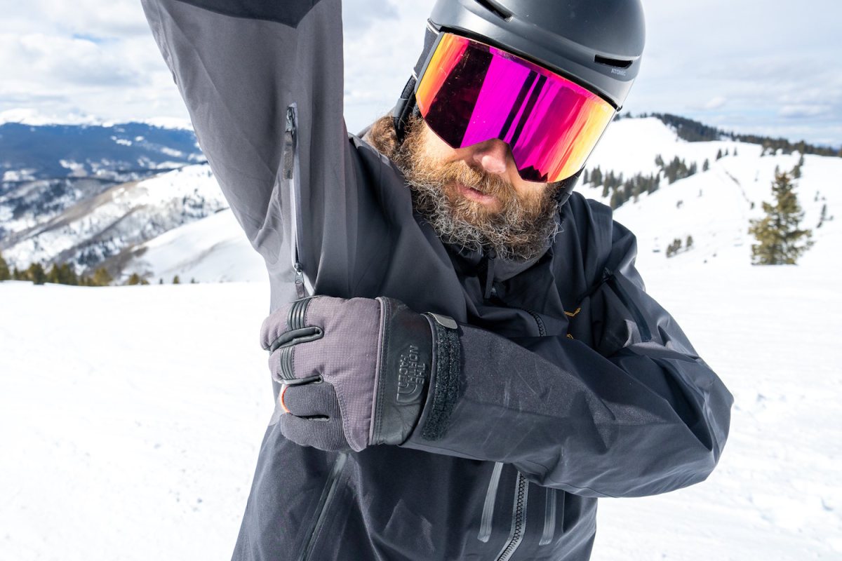 A skier with mirrored goggles raises an arm to demonstrate the large underarm pit zip on the Arc'teryx Rush jacket