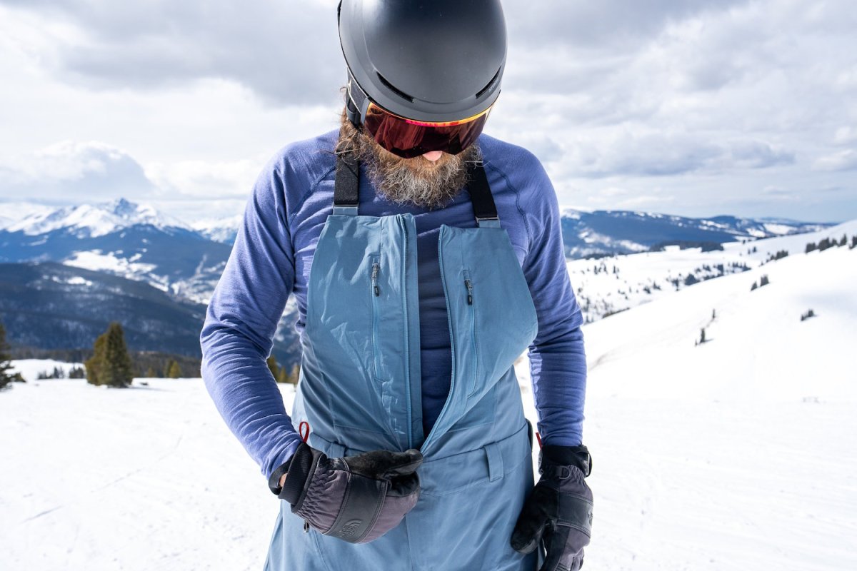 Skier wearing Black Diamond Recon Bibs partially unzipped to show base layer, highlighting front zipper and chest pocke