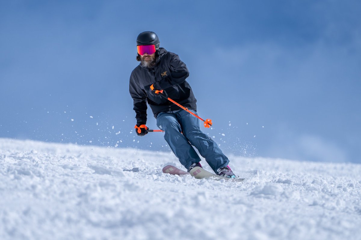A skier in a black jacket wearing blue Recon bibs carving through soft snow.