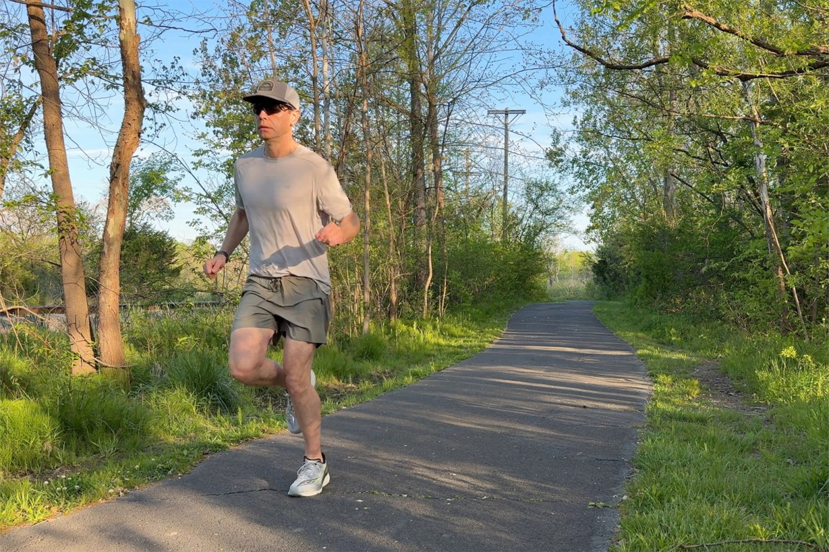 Runner wearing gray shoes on a shaded paved path through trees