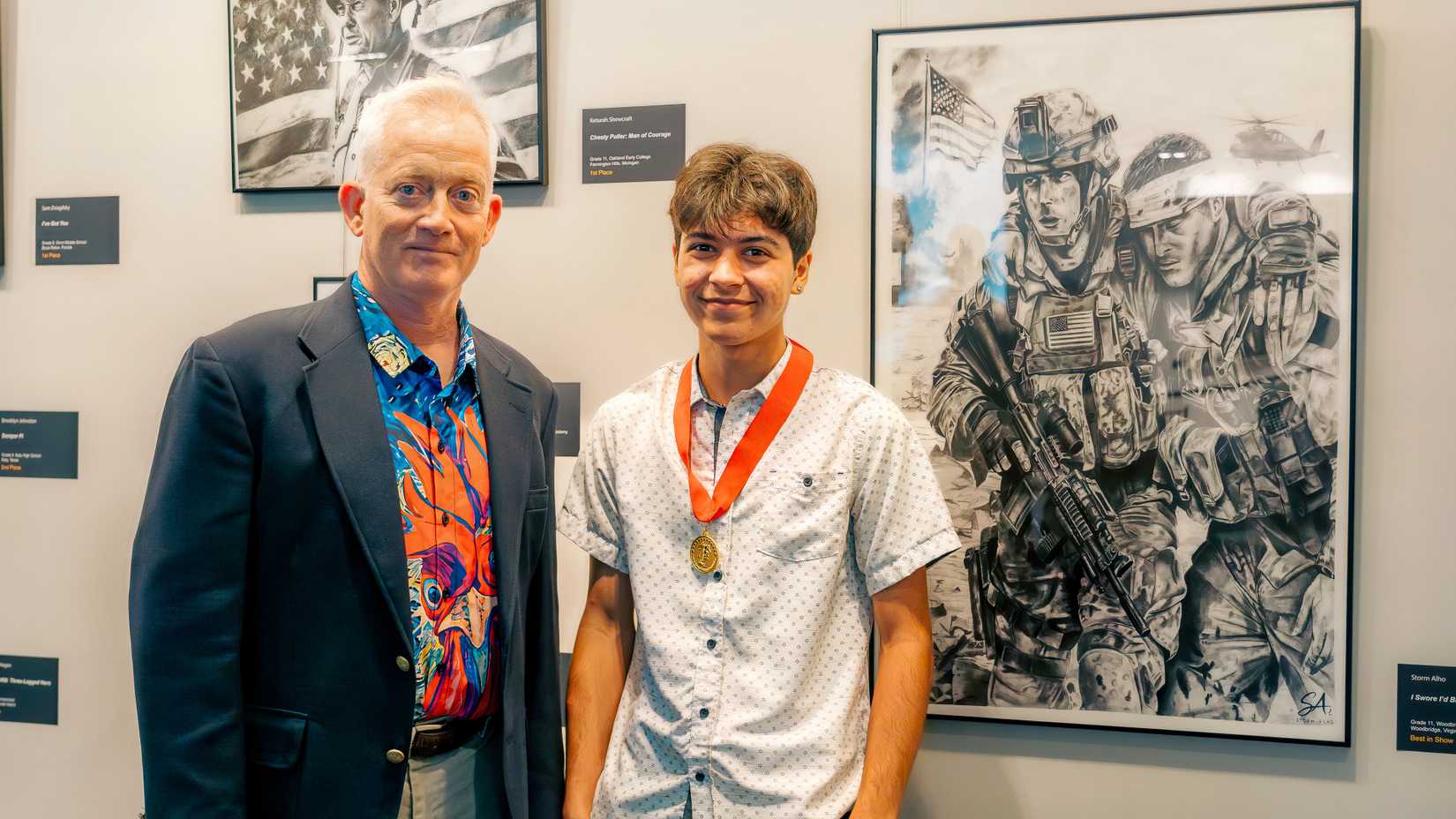 Marine Corps Artist in Residence Kris Battles stands with student artist Storm Alho beside the Best in Show artwork.
