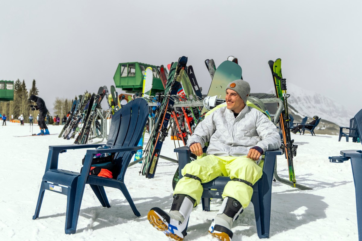 Rider sitting on a chair in the snow wearing Burton Highshot snowboard boots with skis and snowboards in the background