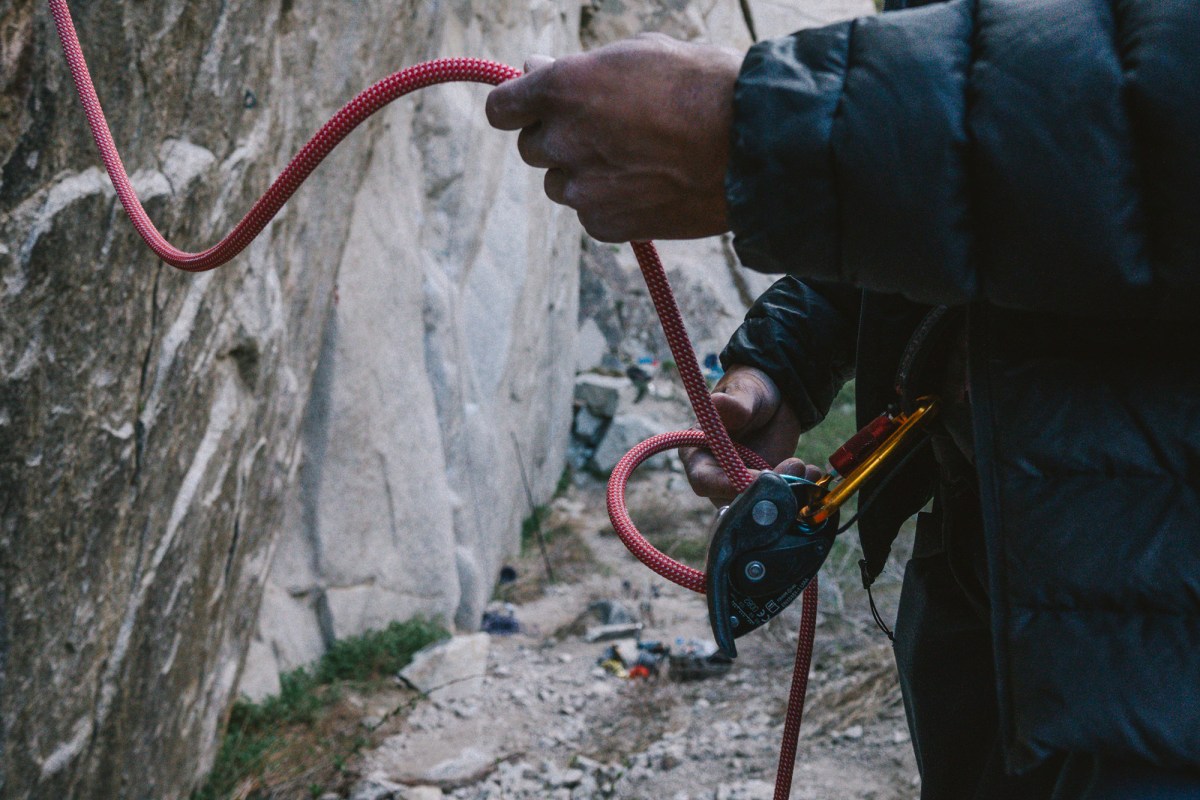 Close-up of a belayer feeding the red rope through a belay device