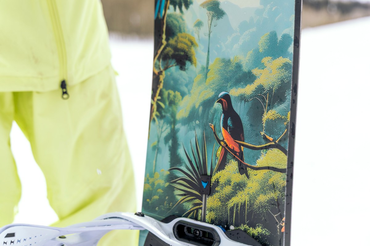 A close up of the Burton Custom Flying V snowboard showing the top sheet graphic near the binding