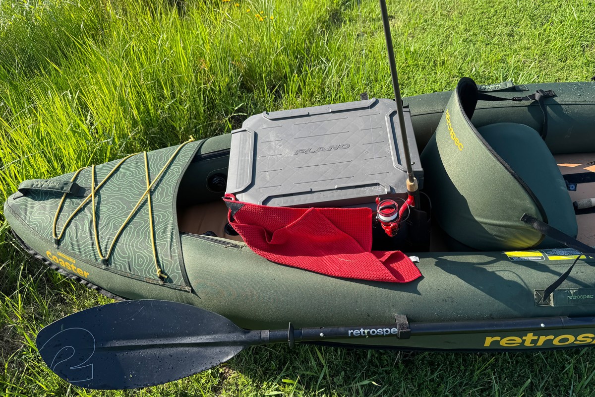 Coaster kayak with paddle, fishing rod, cooler, and gear on the grass