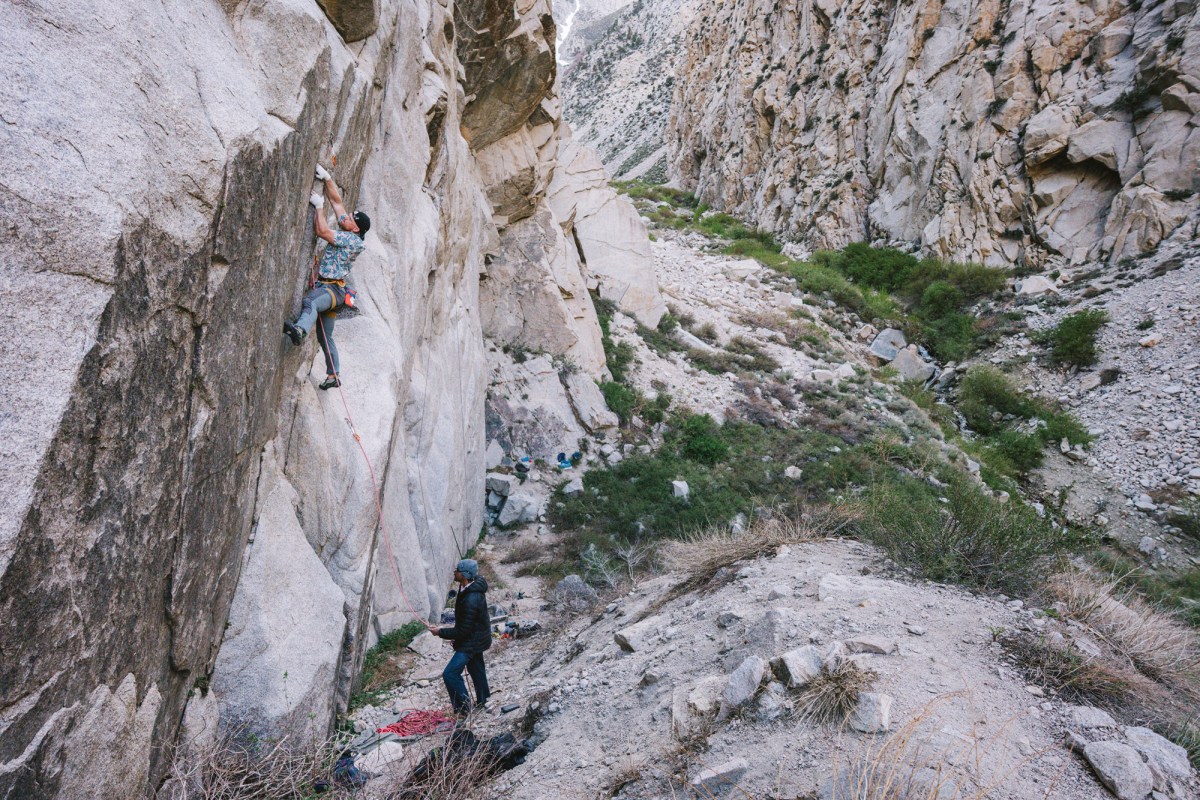 Climber on a granite wall while a belayer manages the rope below