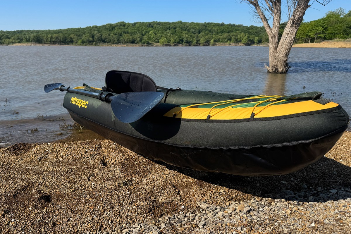 Green Retrospec Coaster kayak with paddle on a gravel lakeshore