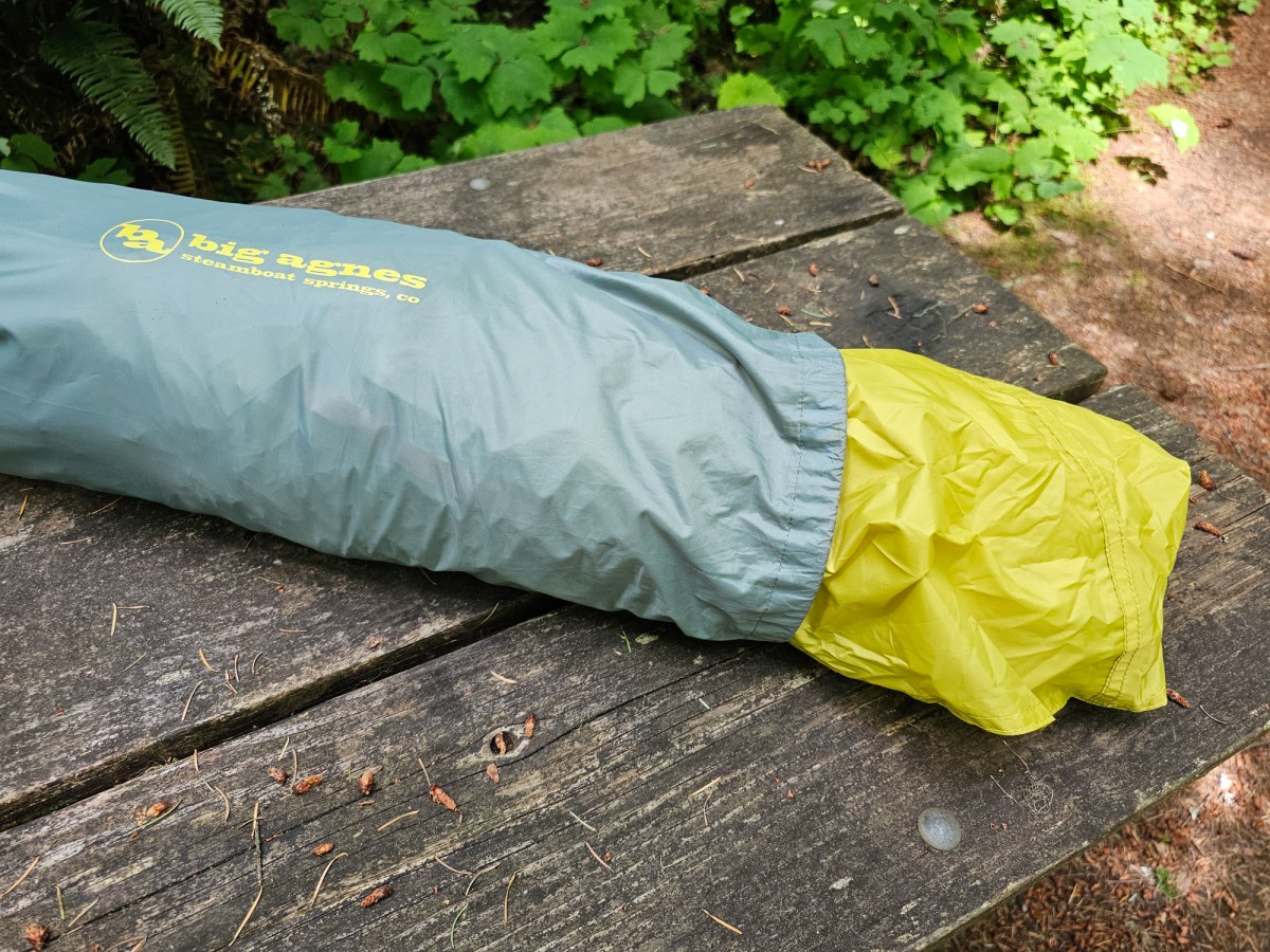 the yellow rainfly of the big agnes blacktail 2 tent sticks out of the grey stuffsack on a picnic table