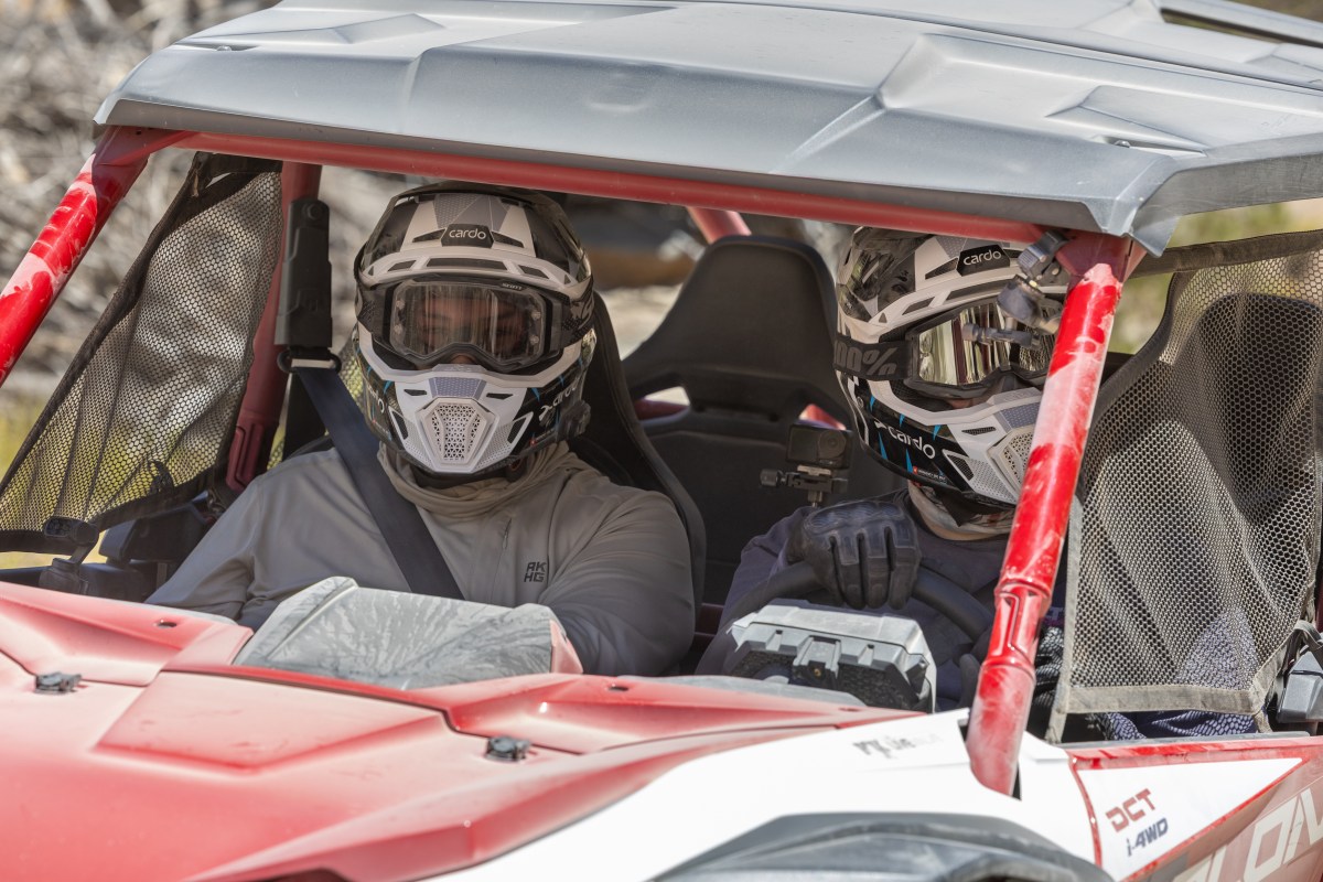 Two riders in a red and white UTV both wearing Cardo Venture helmets.