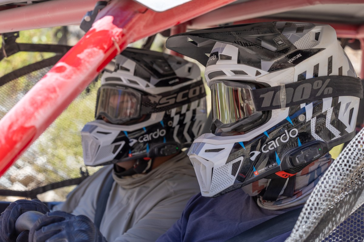 Two men in helmets sit in a red side-by-side