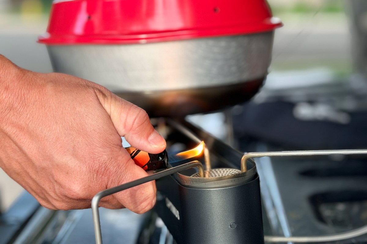 A hand uses a lighter to ignite the burner on the Optimus Gemini II dual-burner stove with a pot above it