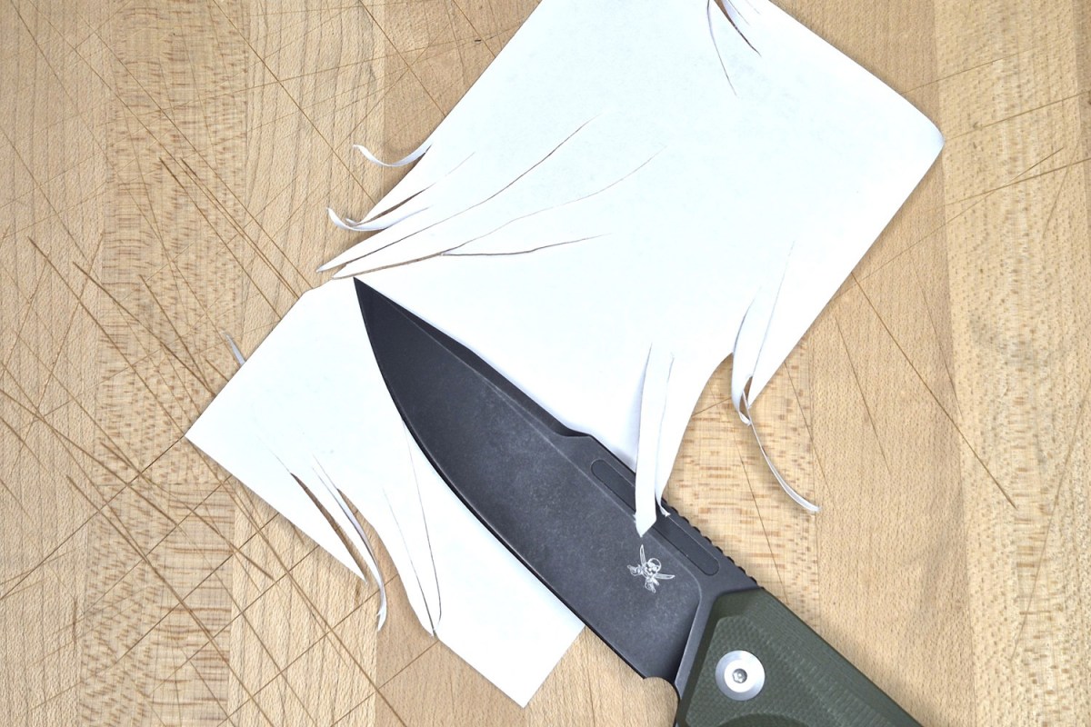Iron Jaw blade cutting through white paper on a wooden surface