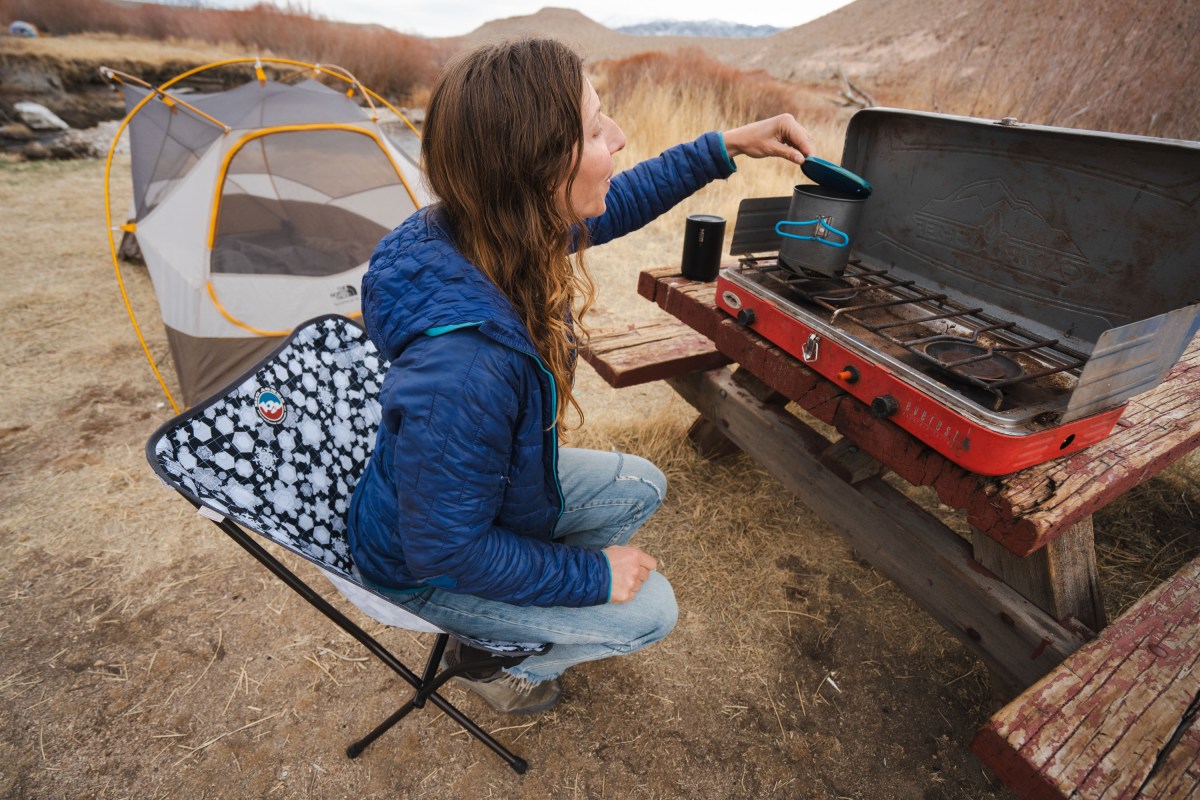 a camper sits up in the taller big agnes mica basin chair to check on a boiling pot of water while camp cooking