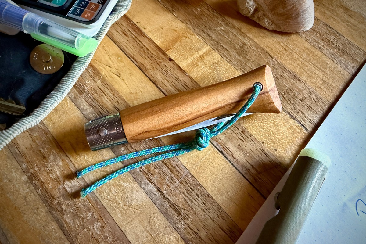 Closed Opinel Néo6 with wooden handle and blue lanyard on a worktable