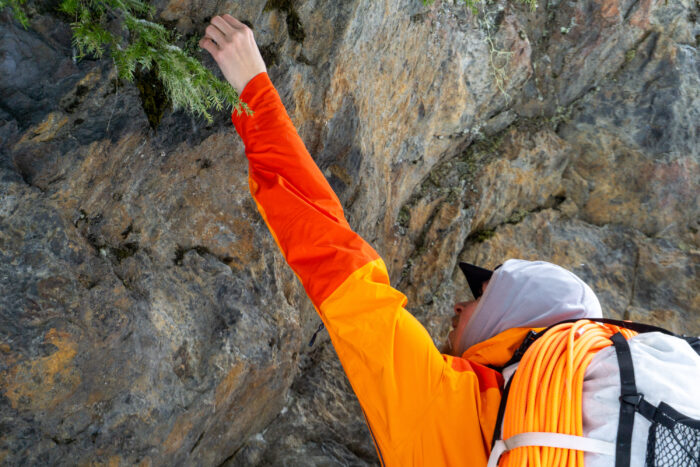 a gearjunkie tester wearing a norona hardshell jacket reaches above for a rock hold