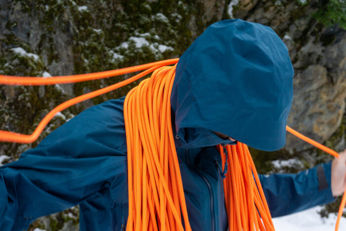 a gearjunkie tester coils a rope over his shoulders while wearing a blue hardshell jacket