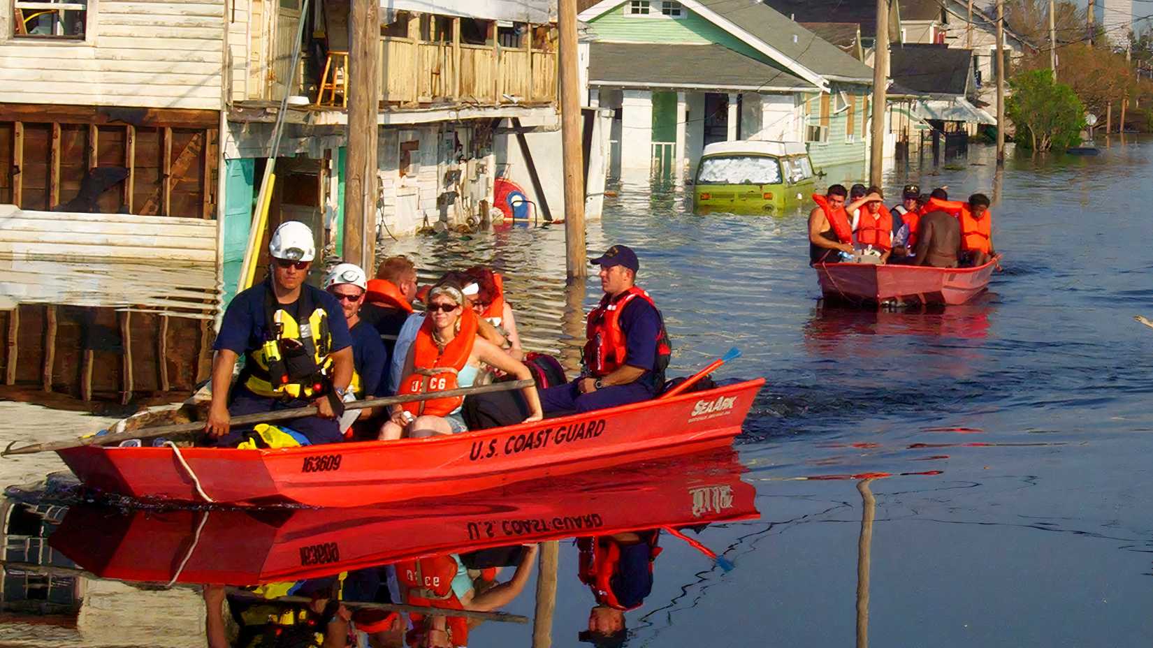 Coast Guard crews carry residents in two red rescue boats through a flooded New Orleans neighborhood after Hurricane Katrina.