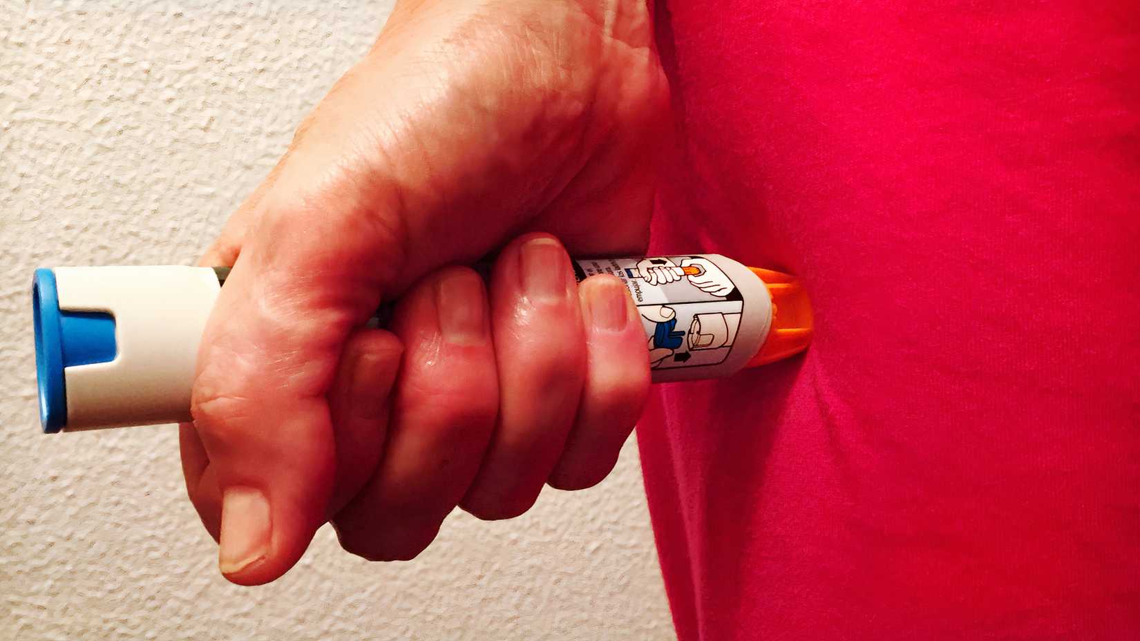 A person holds an epinephrine auto-injector against the outside of their thigh.