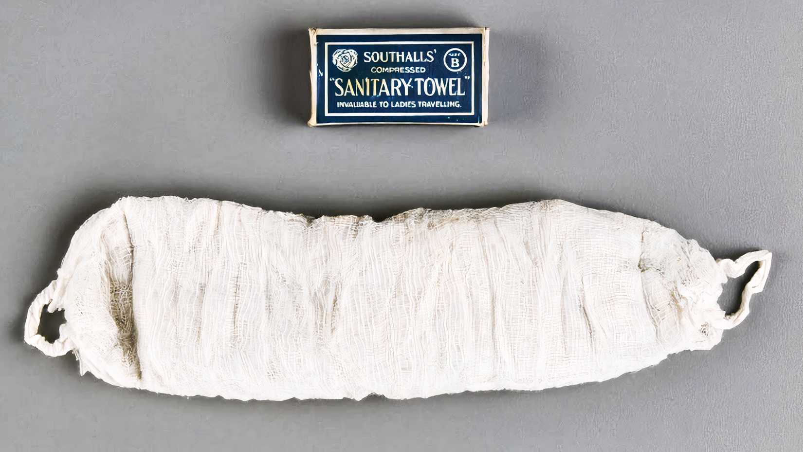 An early gauze sanitary towel lies beneath a small blue-and-white cardboard package.