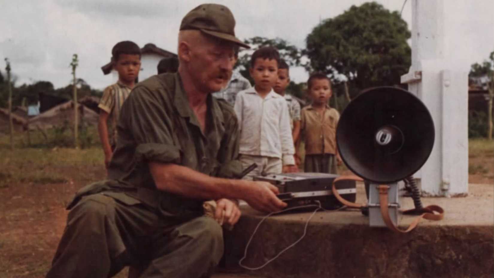 A U.S. Army psychological operations soldier connects a tape recorder to a loudspeaker as Vietnamese children watch.