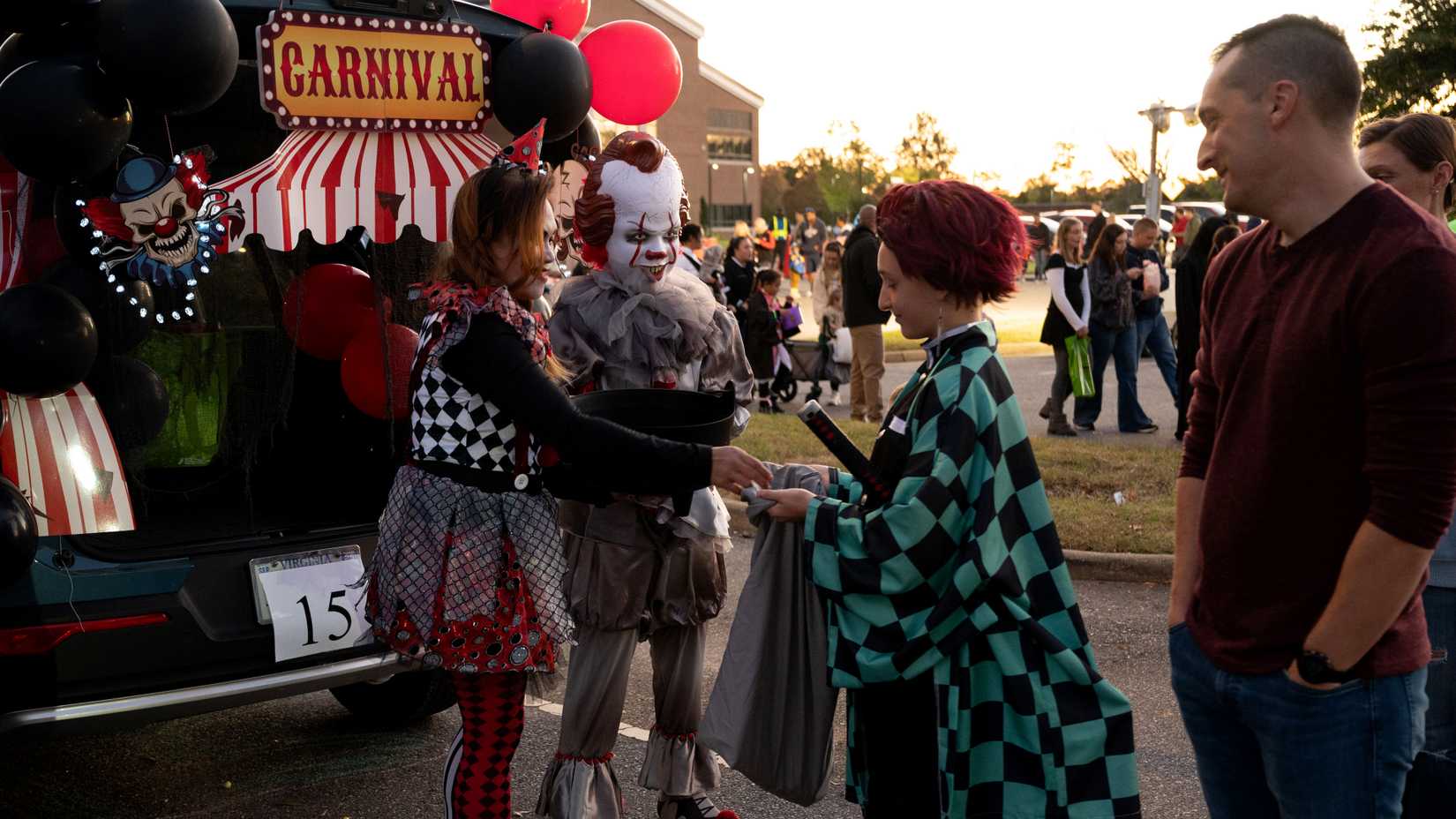 Costumed military families collect candy beside a carnival-themed vehicle at Joint Base Langley-Eustis.